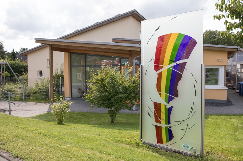 Gartenstele mit Abbildung eines silisierten Regenbogens und zwei Kindern, die sich an der Hand nehmen.