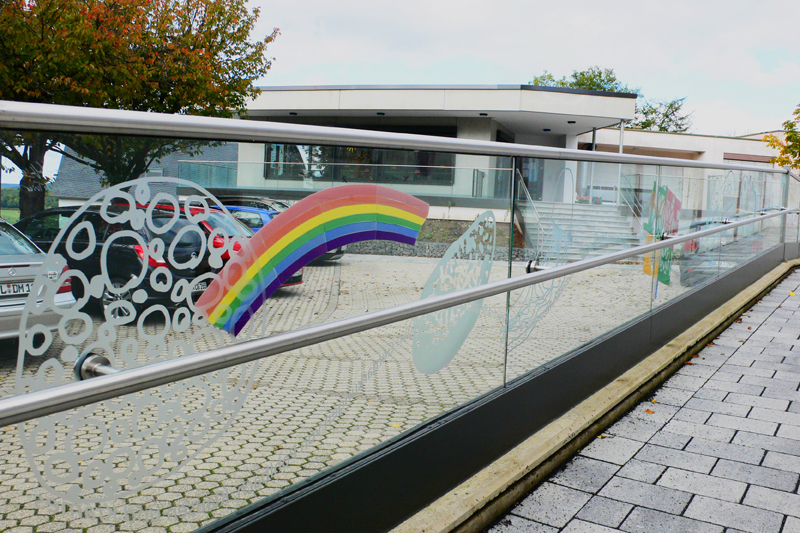 Zaun aus Glas vor den dem Gebäude mit einer Abbildung von einem Regenbogen 