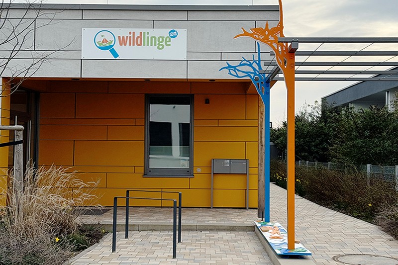 vor dem Kita-Gebäude ist eine Säule künstlerisch gestaltet in Balu und Orange